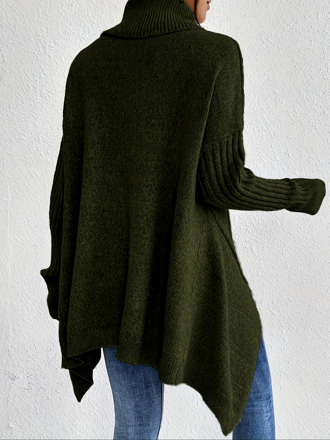 Back view of green turtleneck sweater with ribbed sleeves, worn with jeans, against a white wall.
