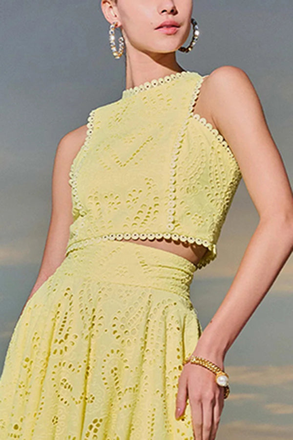 Close-up of a model wearing a yellow embroidered top and skirt set against a sunrise view.
