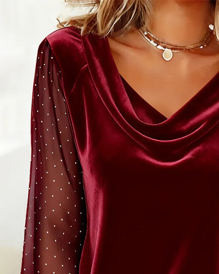 Close-up of maroon blouse with draped collar and sheer polka dot sleeve, indoors.