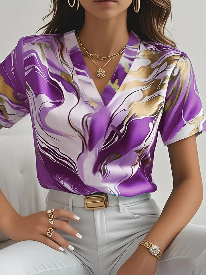 Purple marble print short sleeve shirt with v-neck, worn with white pants and gold accessories in an indoor setting.