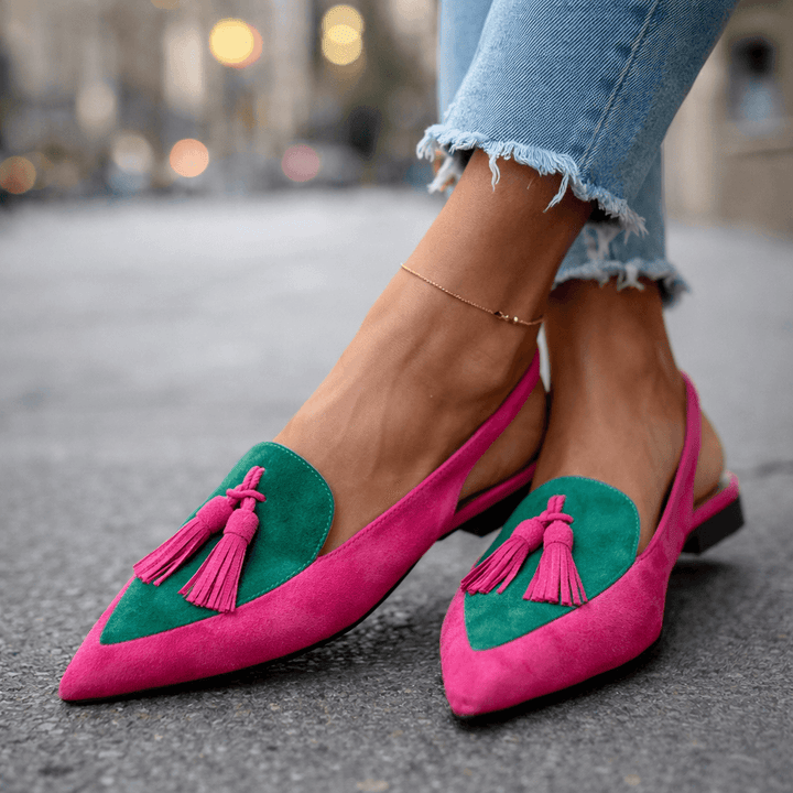 Pink and green sandals with tassels, worn with frayed jeans, urban road.