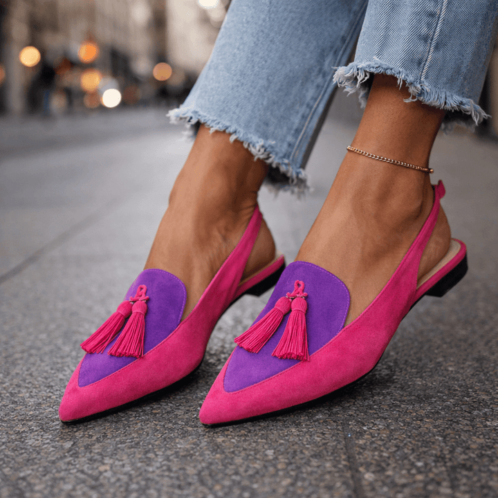 Pink and purple sandals with tassels, worn with jeans, on urban street.
