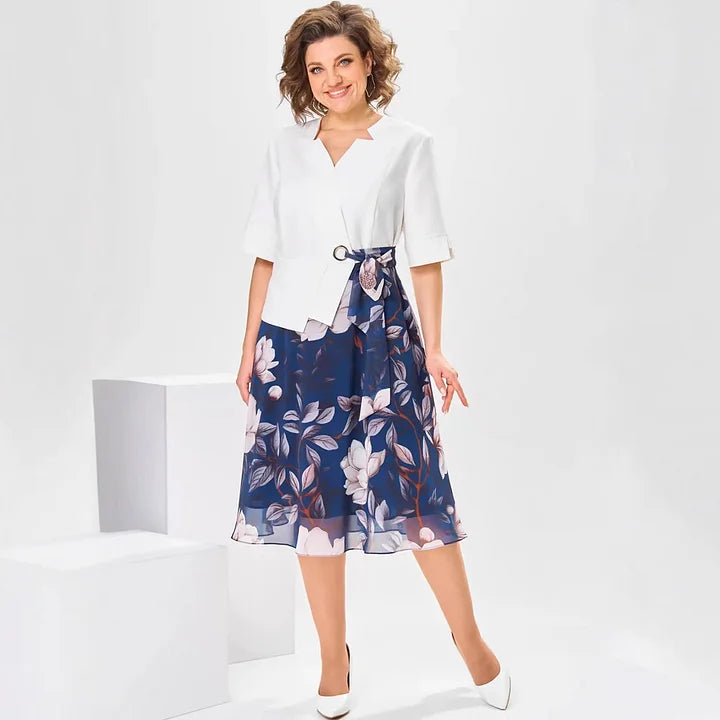 Woman wearing white top and navy floral midi skirt, standing in a minimalist white studio.