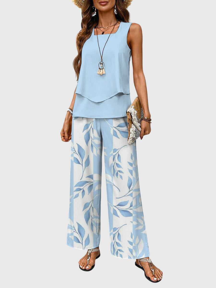 Model in light blue sleeveless top with layered hem and floral wide-leg pants. Neutral backdrop.
