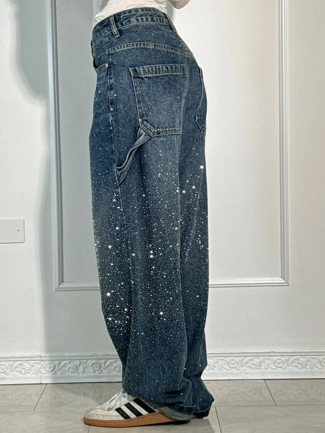 Rear side view of dark blue sparkling trousers with oversized pocket and striped sneakers in a well-lit studio.