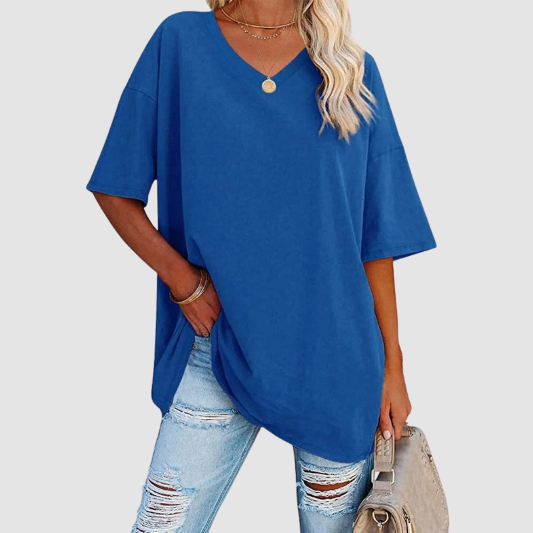 Woman in a blue V-neck T-shirt with distressed jeans, carrying a beige bag, studio setting.