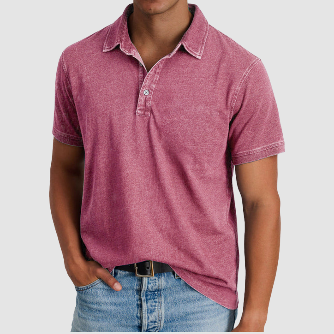 Model featuring a pink classic collared polo with short sleeves, button placket, worn with light jeans, against studio backdrop.
