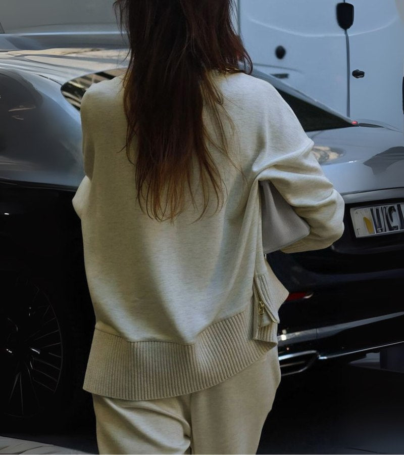 Back view of a woman wearing a cream two-piece set, walking towards a parked black car.