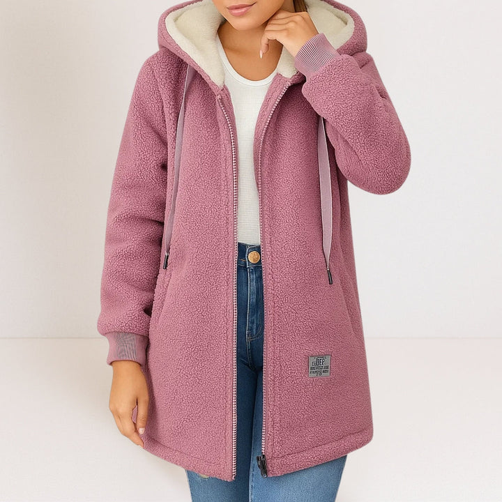 Model wearing a pink soft jacket with a hood and drawstrings, complemented by blue jeans in a light studio environment.