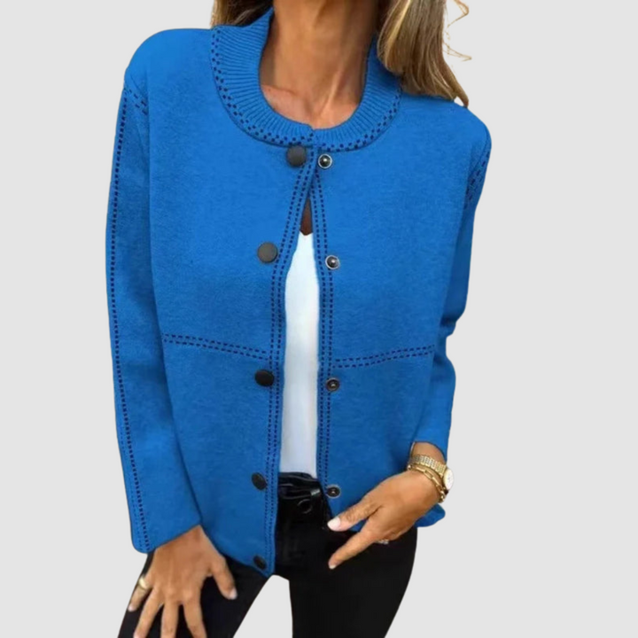 Blue jacket with round collar, button closure, worn over white top and black pants in a studio setting.