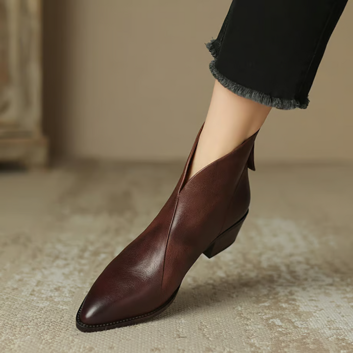Elegant brown ankle boots with pointed toes, styled with black frayed pants on a neutral carpet.