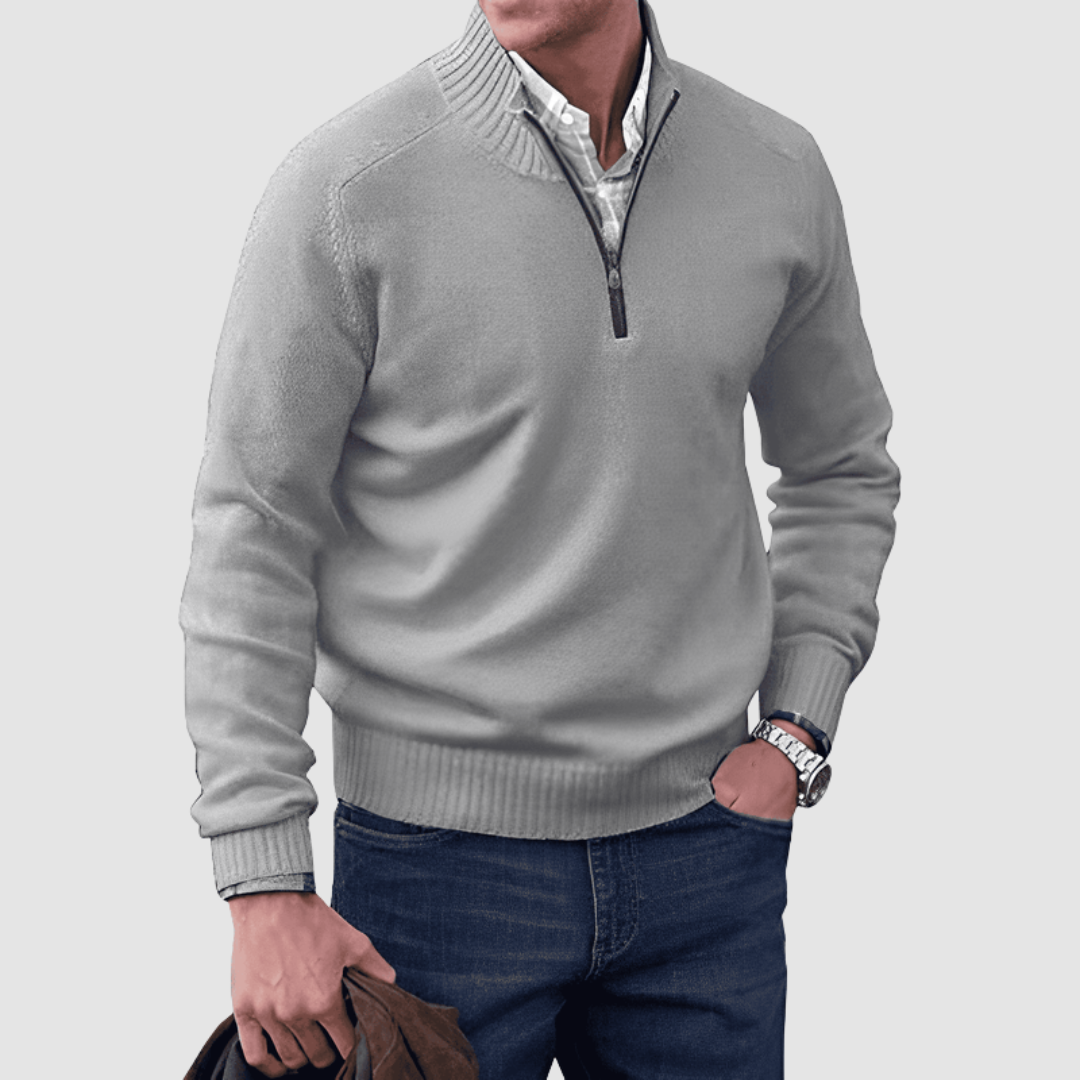 Model in light gray zip pullover with ribbed collar and cuffs, holding a jacket. Paired with jeans, set against a plain background.