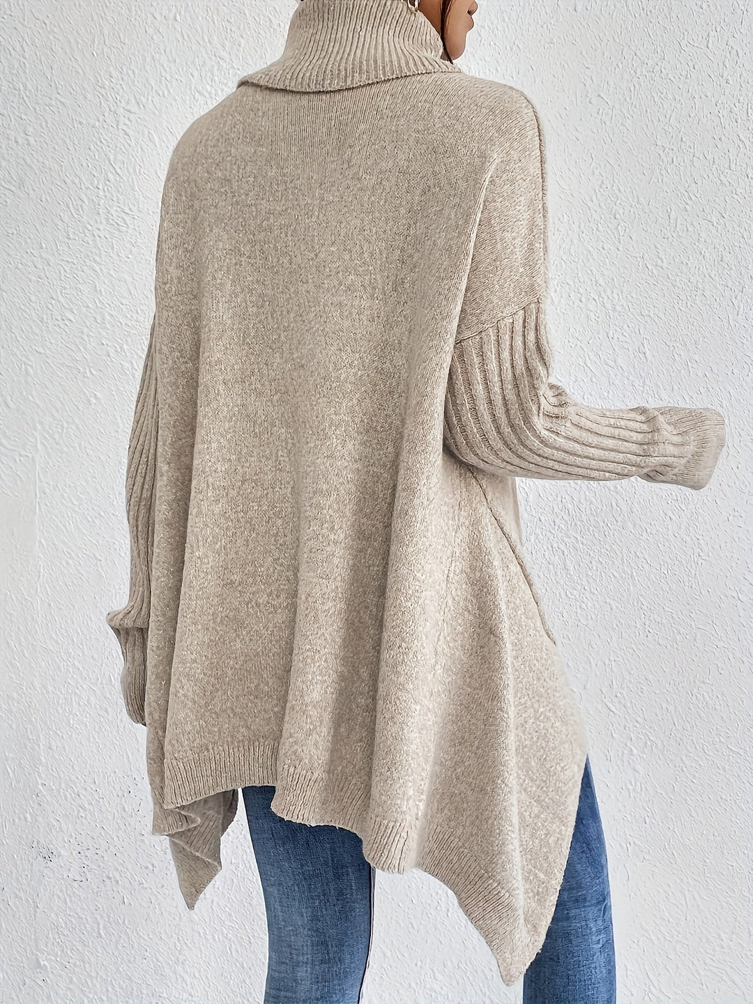 Back view of beige turtleneck sweater with ribbed sleeves, worn with jeans, against a plain white background.
