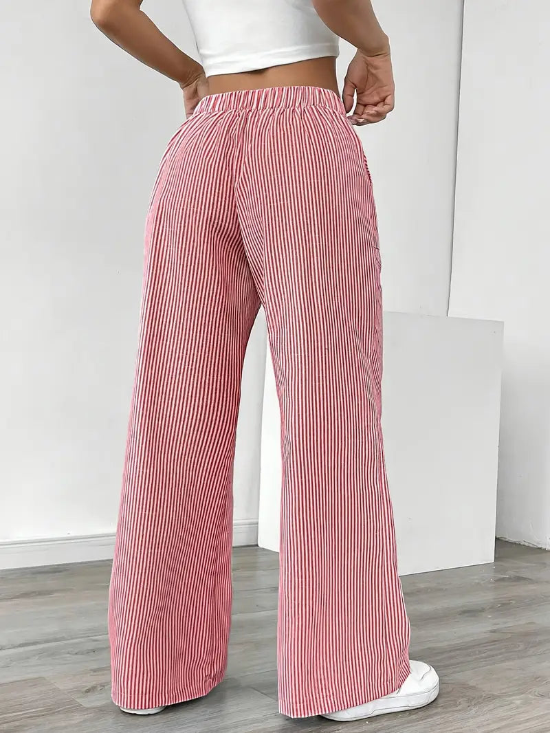Back view of red and white striped relaxed pants with elastic waistband, worn indoors with white sneakers.