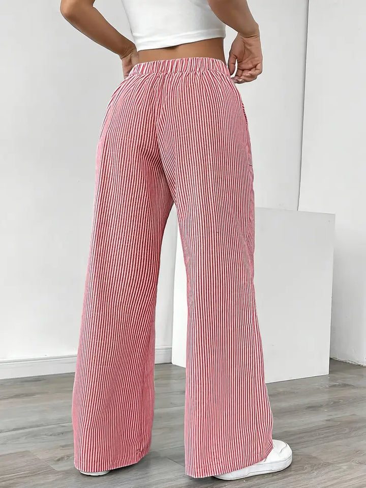 Back view of red and white striped relaxed pants with elastic waistband, worn indoors with white sneakers.