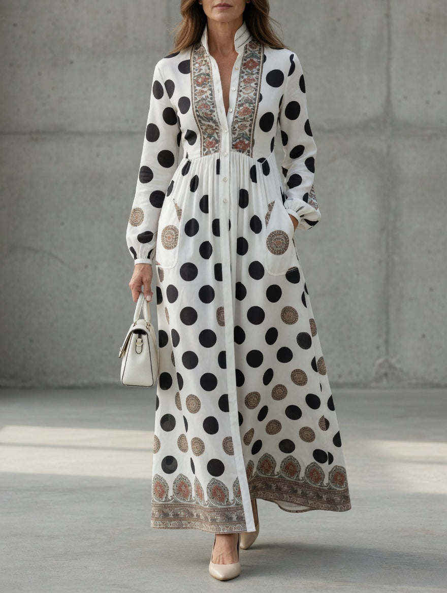 Elegant maxi dress with large black polka dots and intricate patterns, worn with a white handbag and heels in a minimalist setting.