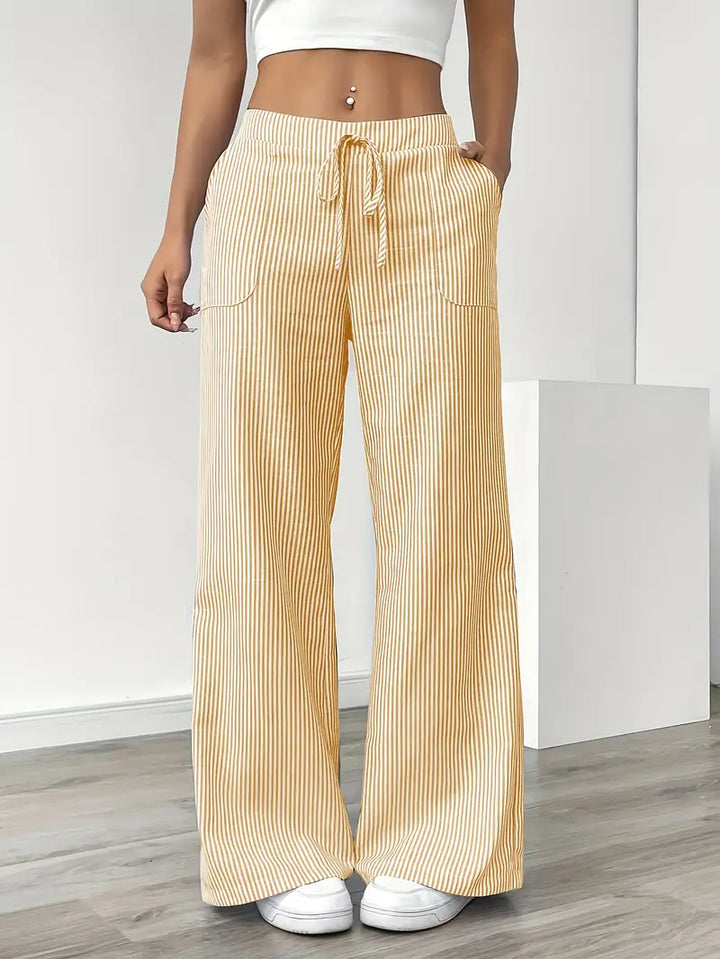 Yellow and white striped relaxed pants with drawstring waist, shown indoors, paired with white sneakers and crop top.