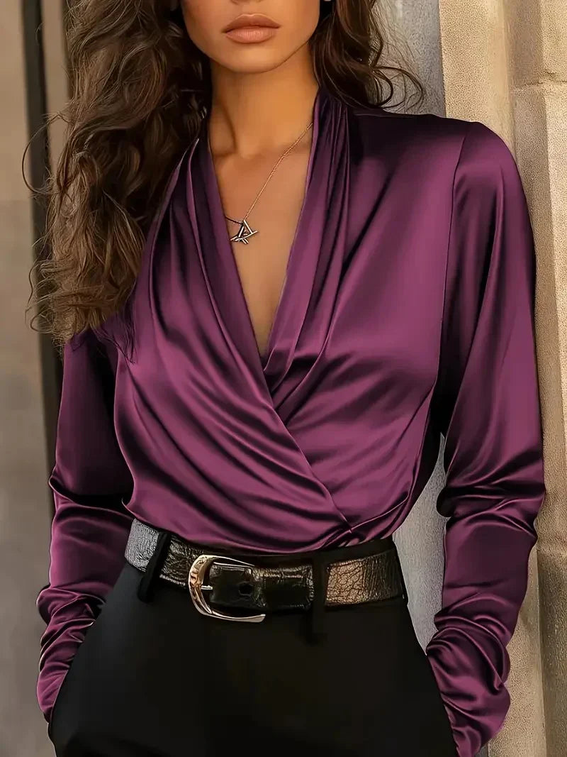 Woman wearing a luxurious purple V-neck top with a draped front, paired with black pants and a belt, in an urban setting.