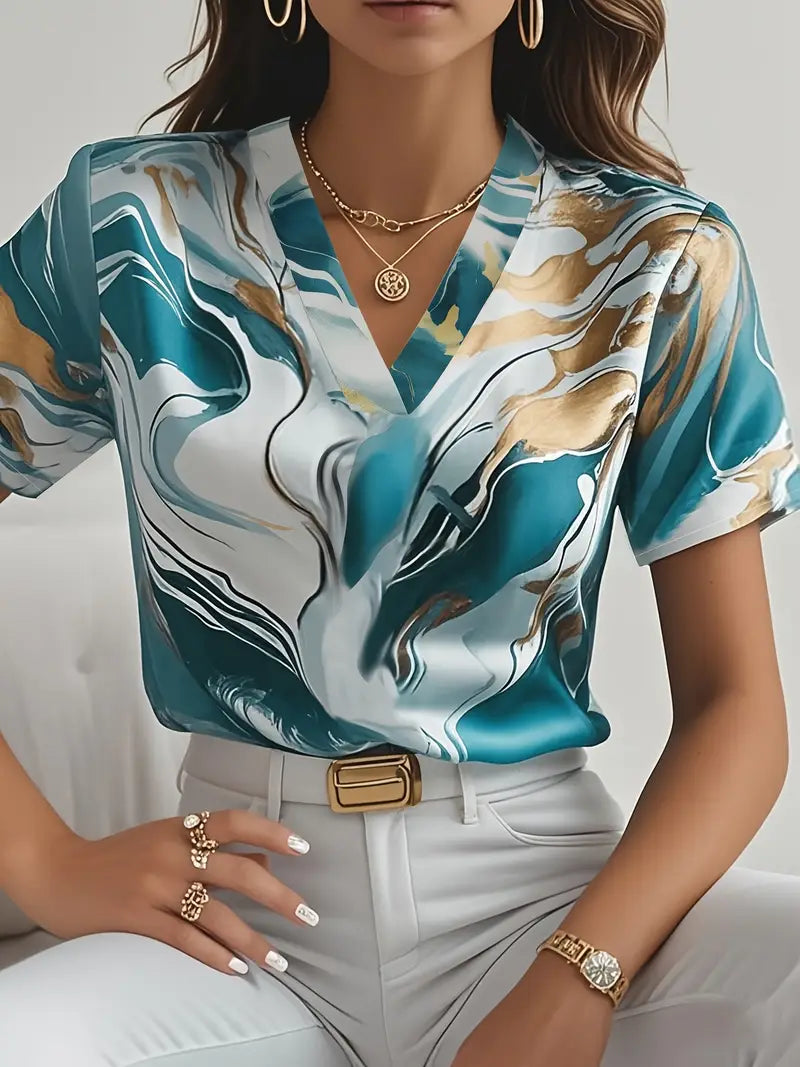 Teal marble print short sleeve shirt with v-neck, worn with white pants and gold accessories in an indoor setting.