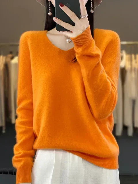 Person in a bright orange loose knit sweater, posing in a fashion studio.