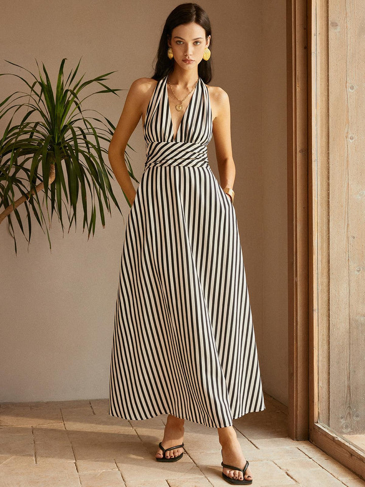 Woman in black and white striped backless dress, standing indoors by a plant, wooden door visible.