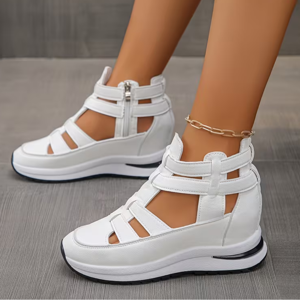 White orthopedic comfort sandals with strappy design and zipper, worn on a wooden floor.