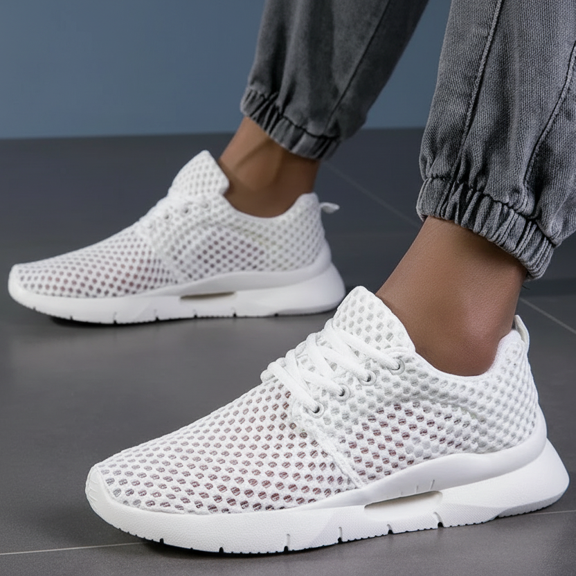 White orthopedic sneakers with mesh design worn with gray joggers on tiled floor.