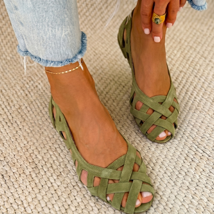 Green comfort sandals with woven design worn on a carpeted floor, paired with light denim jeans.