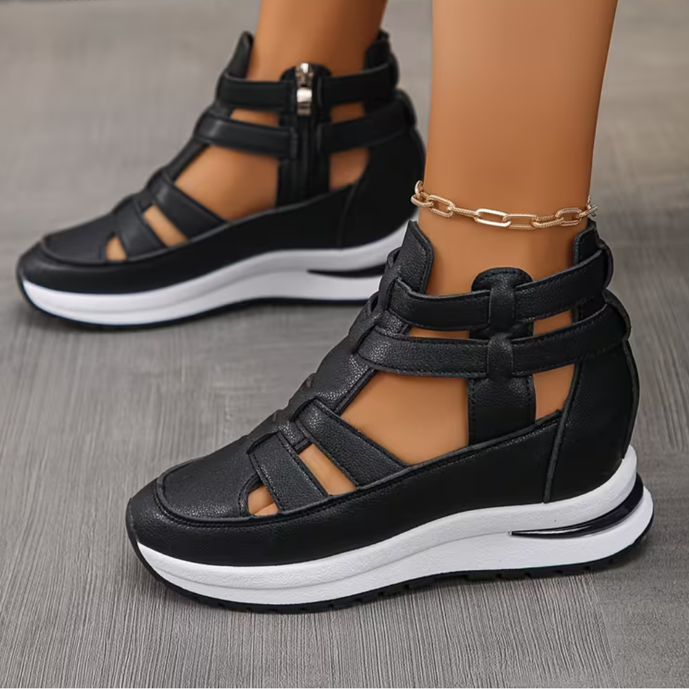 Black orthopedic comfort sandals with strappy design and zipper, worn on a wooden floor.