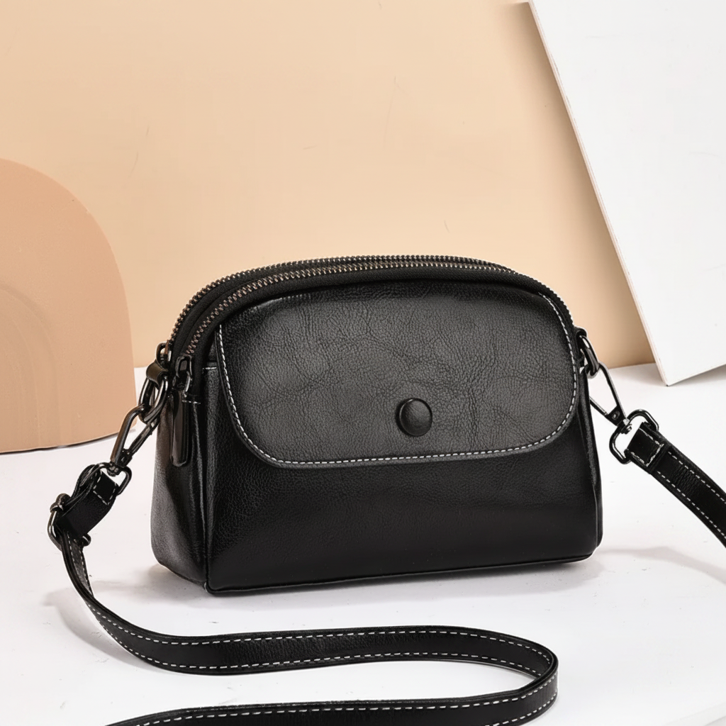 Black crossbody bag featuring a front pocket and adjustable strap, displayed on a beige backdrop with abstract shapes.