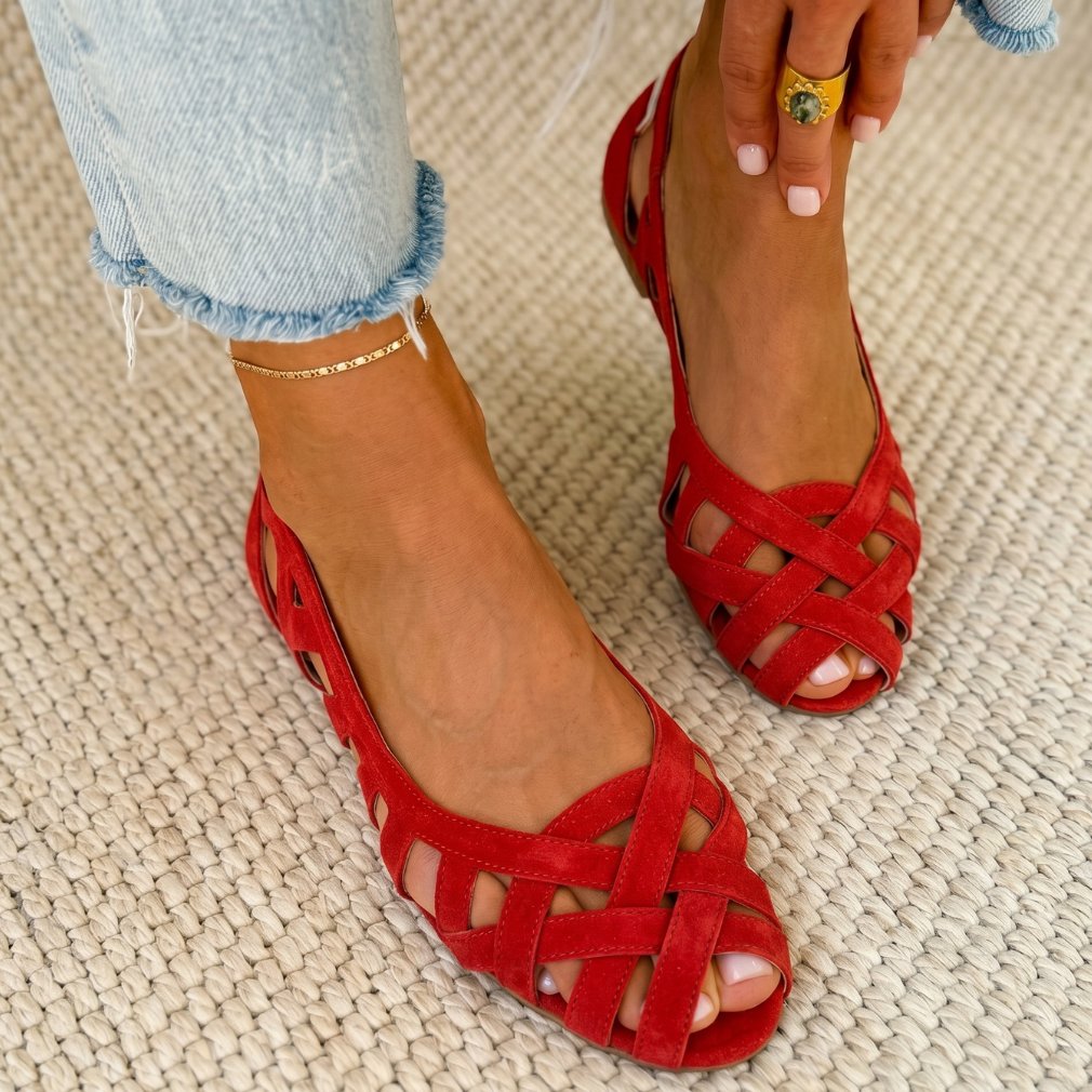 Red comfort sandals with woven design worn on a carpeted floor, paired with light denim jeans.