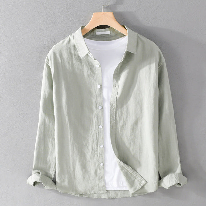 Muted green shirt over white tee on hanger against gray wall.
