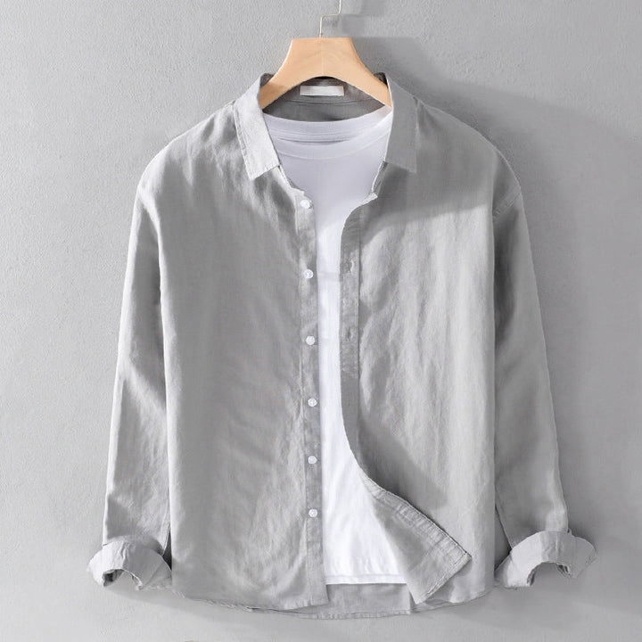 Light gray shirt over white tee on hanger against gray wall.