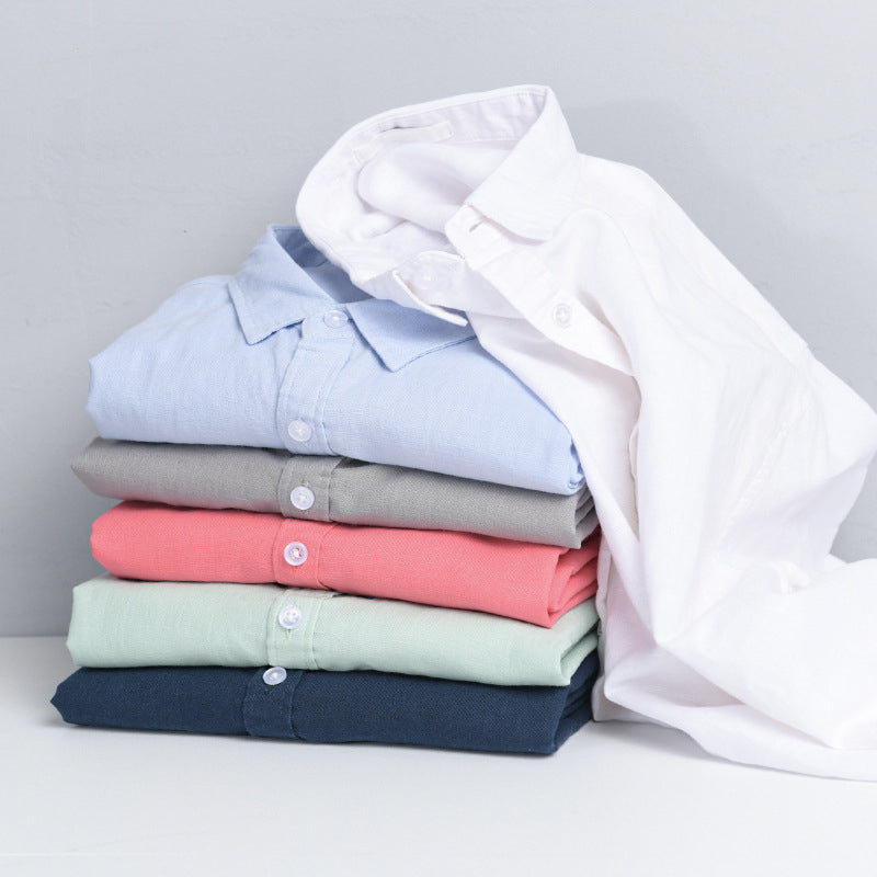 Stack of folded shirts in various colors on white surface.