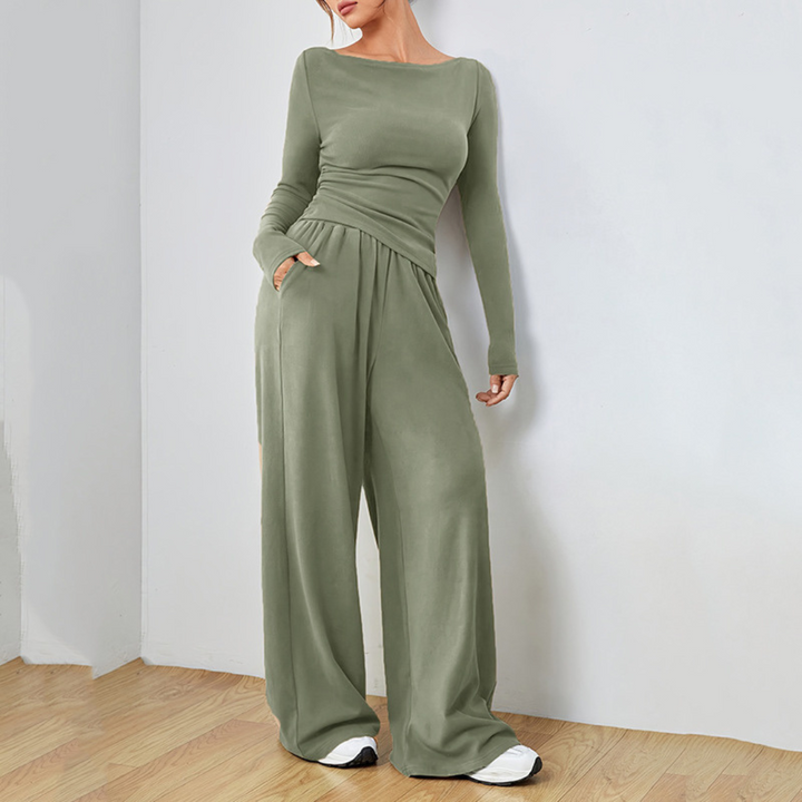 Model wearing olive green comfortable set with a long-sleeve top and wide-leg pants in a plain room with light walls and wood floor.
