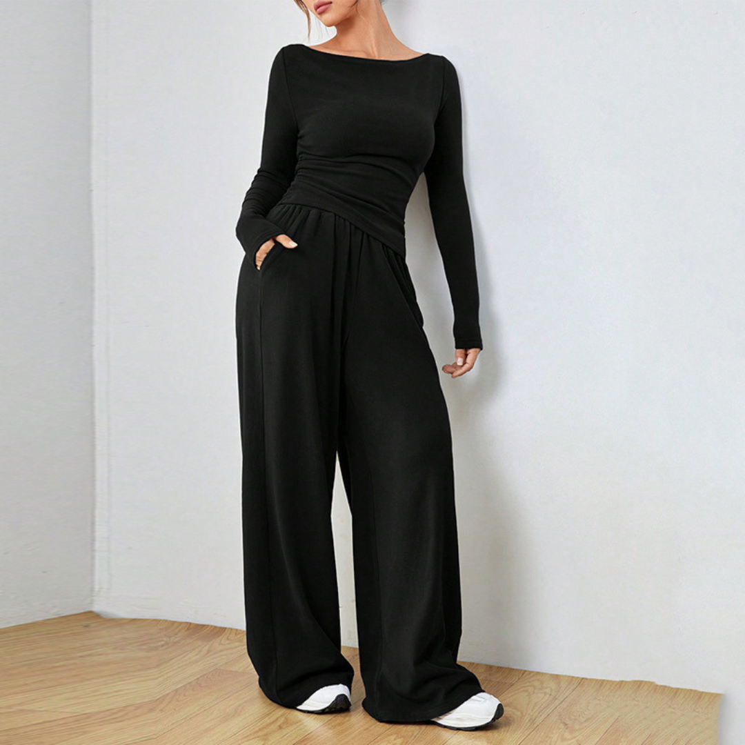 Model wearing black elegant cozy set with a long-sleeve top and wide-leg pants in a serene indoor space with wooden flooring.