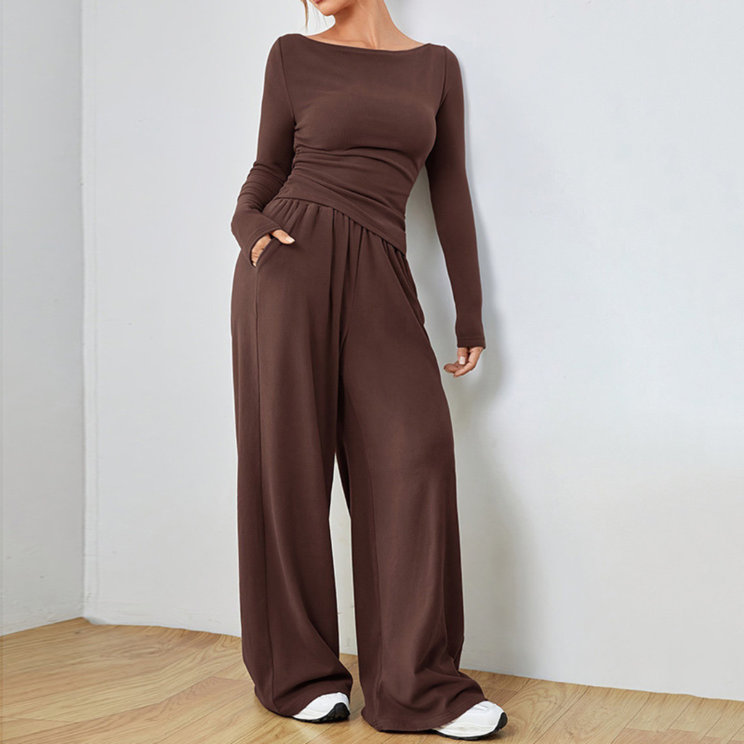 Model in a deep brown cozy set, featuring a long-sleeve top and wide-leg pants, in a minimalistic room with wood flooring.