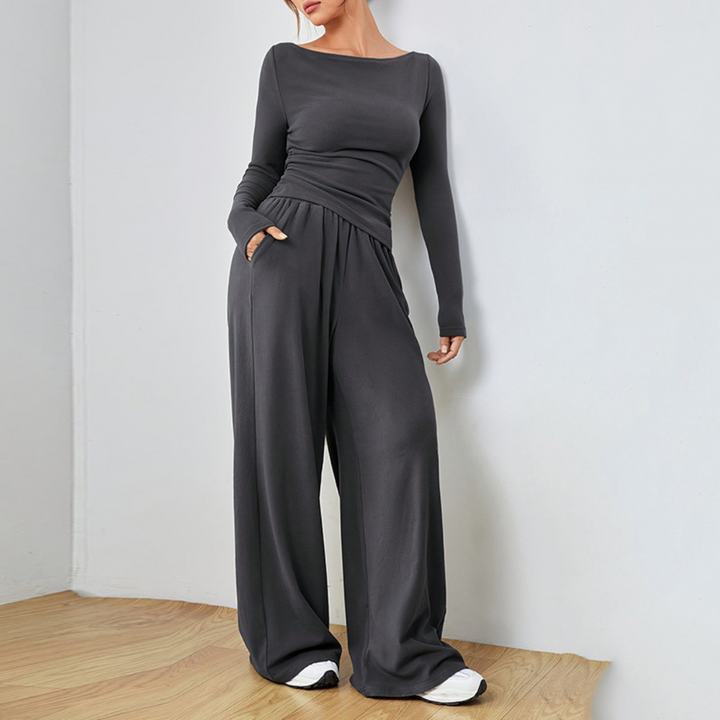 Model in a dark charcoal cozy set featuring a long-sleeve top and wide-leg pants, posed in a simple room with wooden floor.