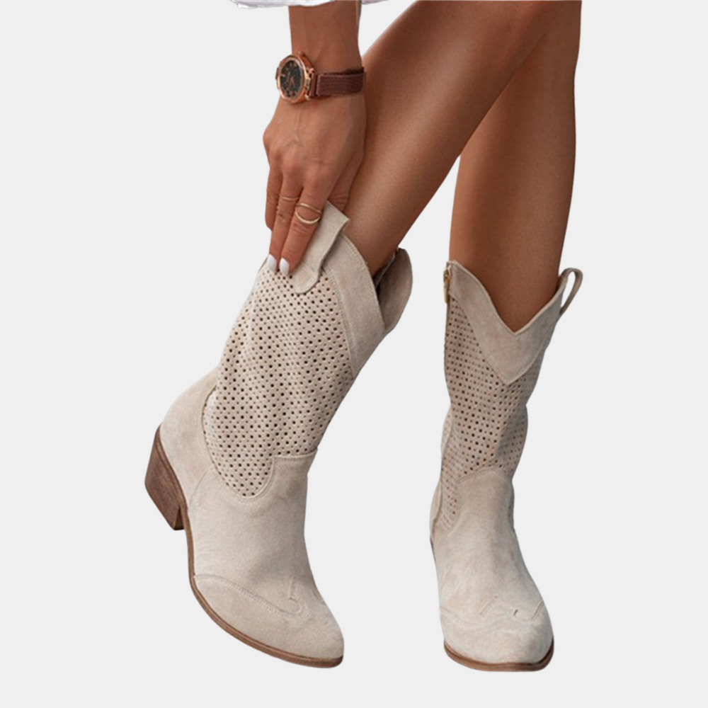 Beige perforated cowboy boots with wooden heels, person adjusting boot against white background.