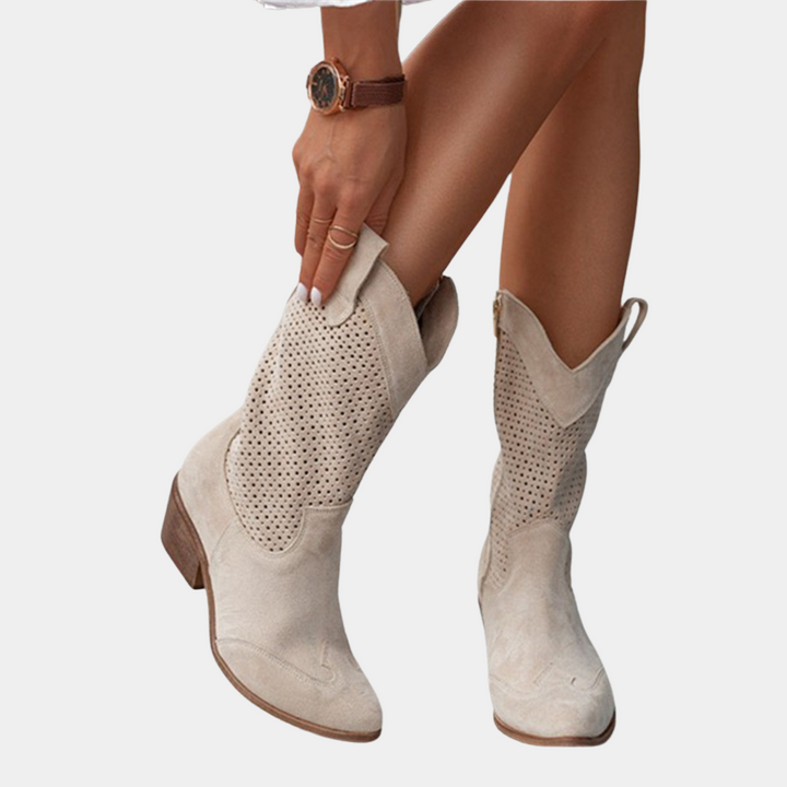 Beige perforated cowboy boots with wooden heels, person adjusting boot against white background.