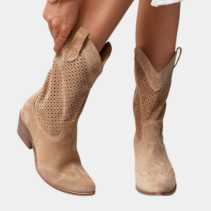 Brown perforated cowboy boots with wooden heels, person adjusting boot against white background.