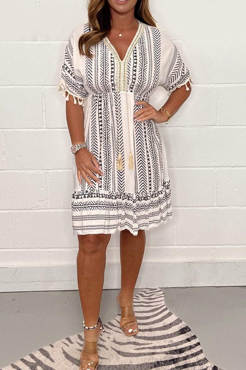 White dress with black patterns and V-neck, worn by woman standing on zebra print rug, white brick background.
