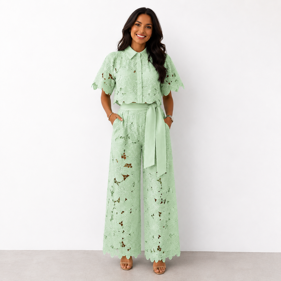 Woman in green floral lace set with wide-leg pants standing against a white studio background.