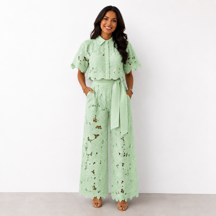 Woman in green floral lace set with wide-leg pants standing against a white studio background.