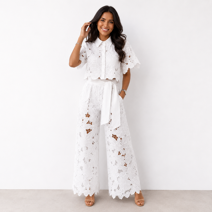 Woman in white floral lace set with wide-leg pants posing against a plain white studio background.