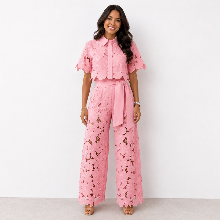 Woman in pink floral lace set with wide-leg pants posing against a white studio background.