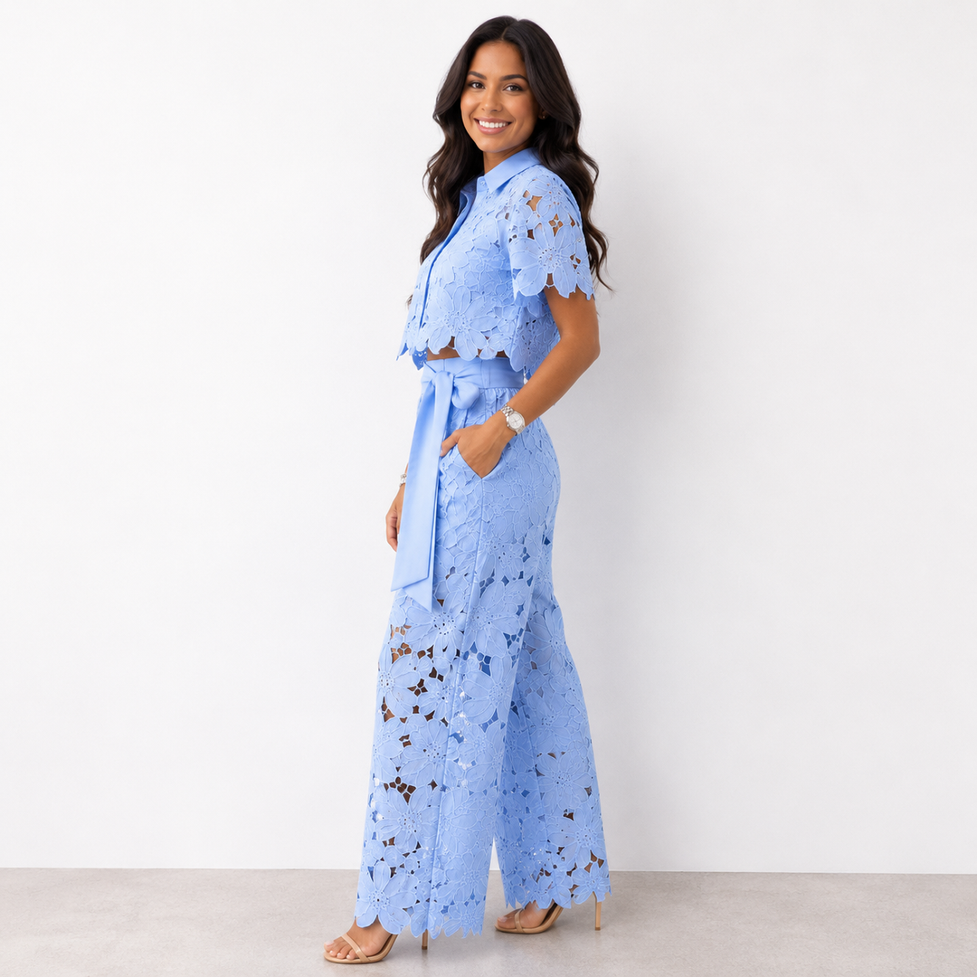 Woman in blue floral lace set with wide-leg pants posing in profile against a white studio backdrop.