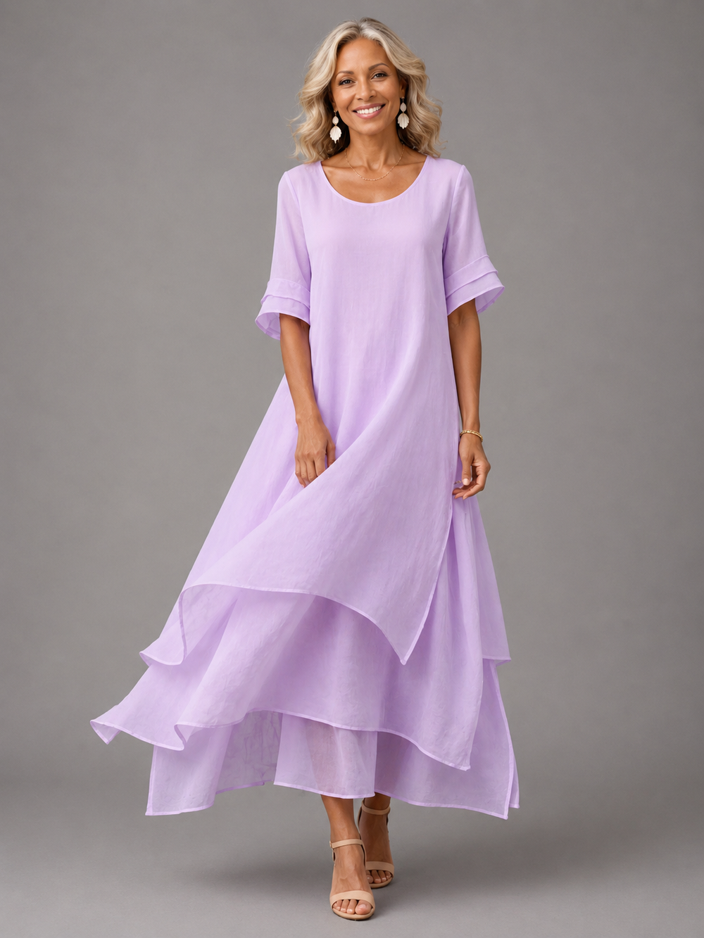 Woman in light purple flowing maxi dress with layered hem, posing in studio, smiling.