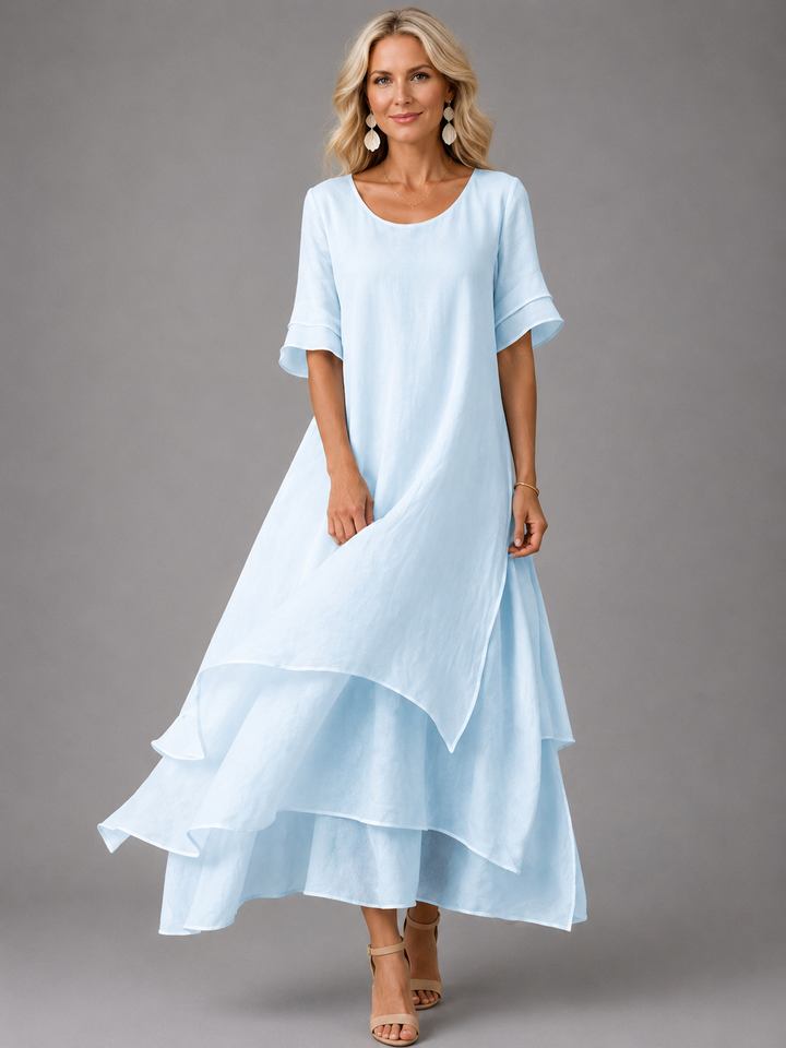 Woman in pale blue flowing maxi dress with layered hem, in a studio setting, smiling.