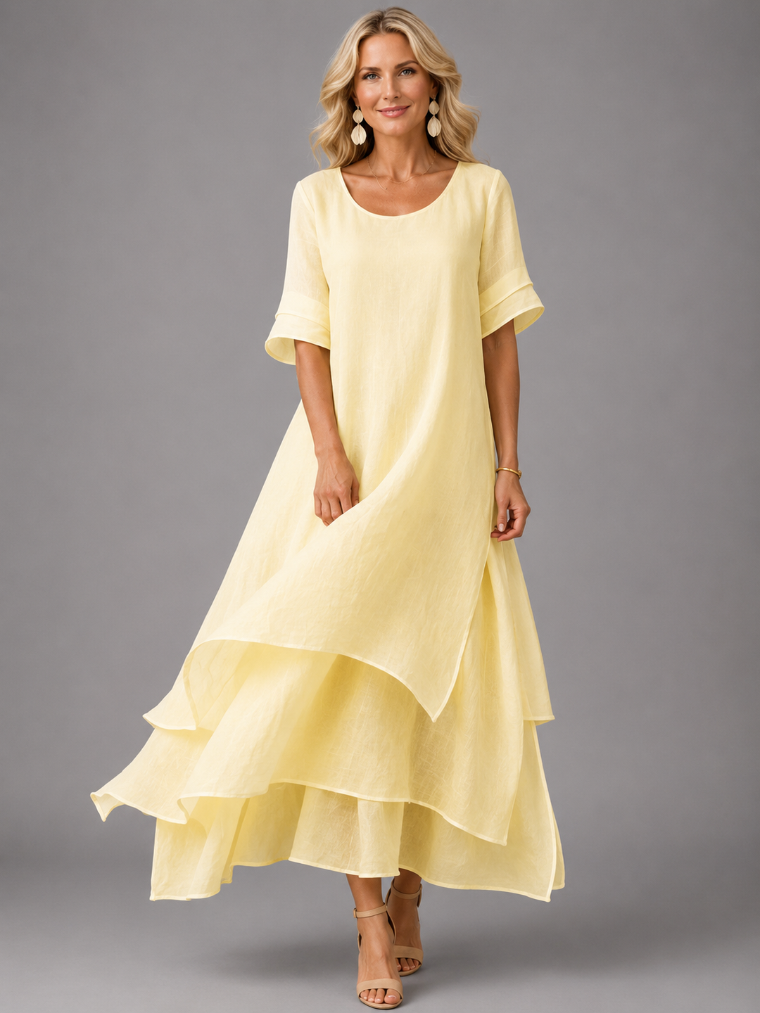 Woman in light yellow flowing maxi dress with layered hem, standing in studio, smiling.